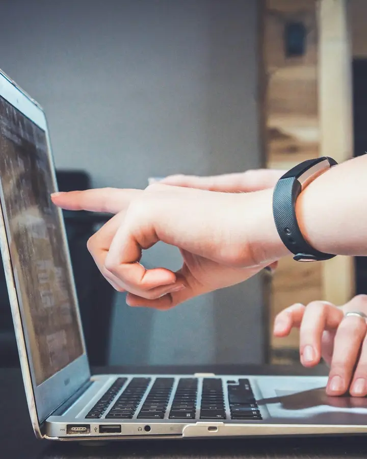 Hands on a laptop keyboard, one pointing at the screen